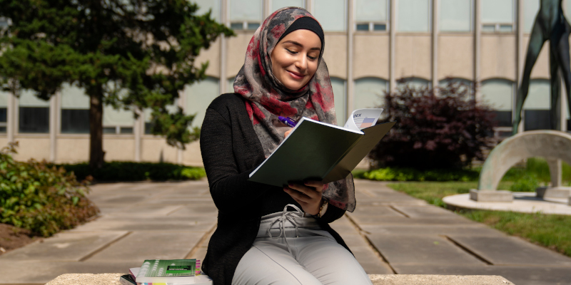 Woman in a Hijab reading a document in front of the faculty of education building